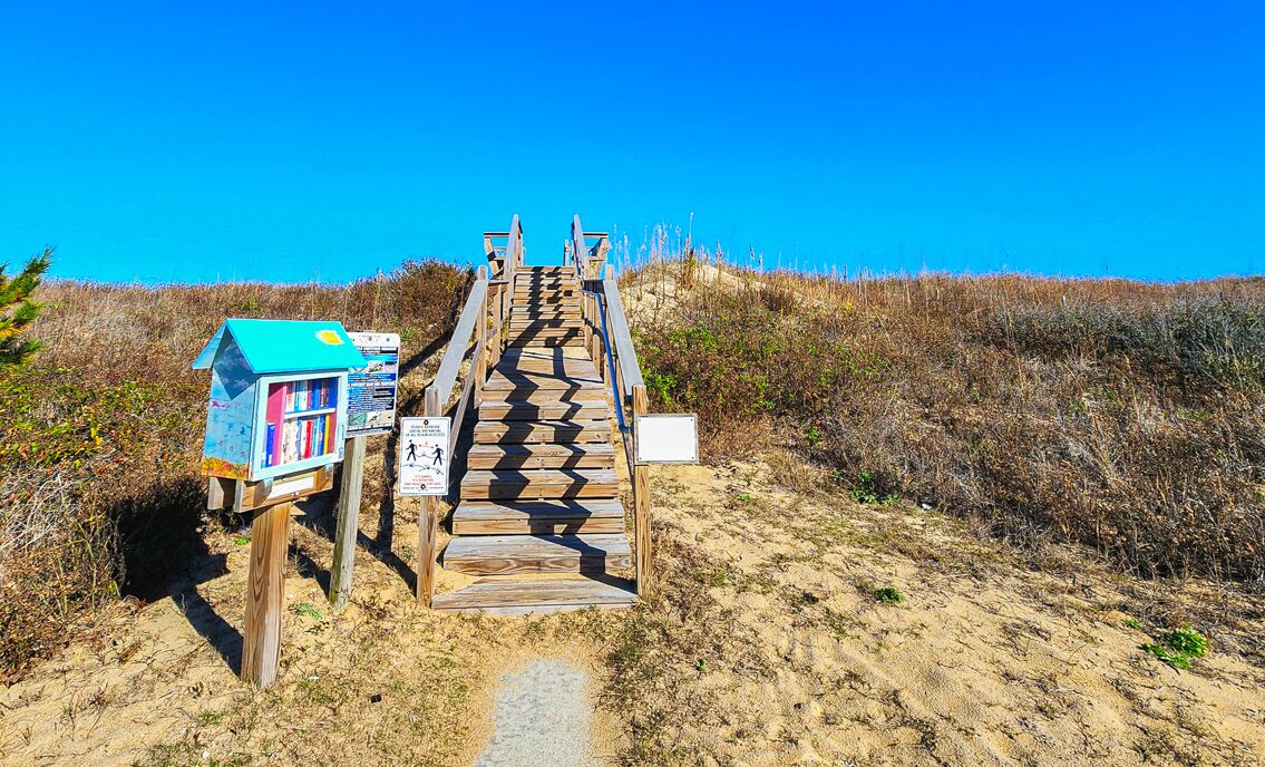 A wooden staircase leading to a beach area with a small blue structure and informational signs.