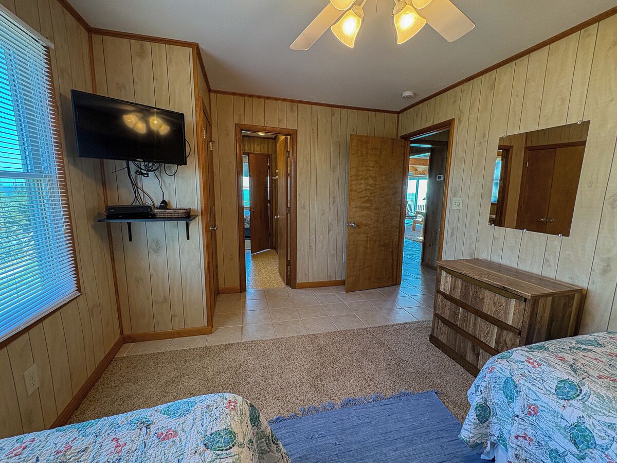 A room with wooden paneling, a television mounted on the wall, a bed with a floral bedspread, and a dresser.