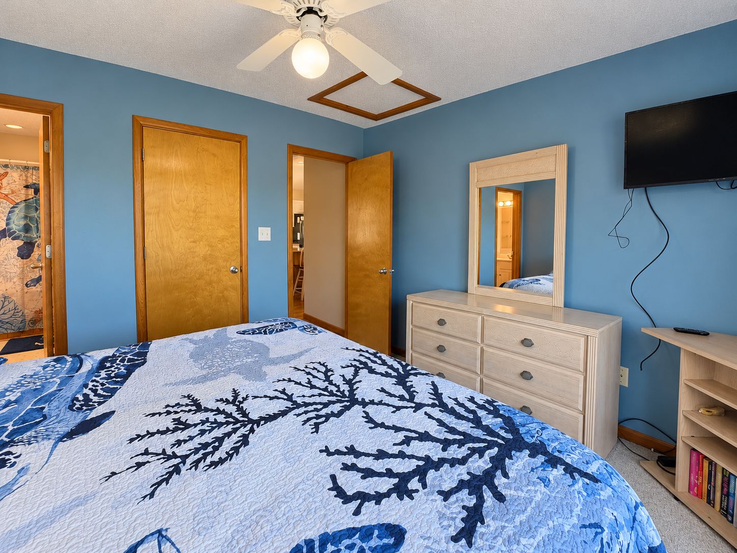Une chambre à coucher avec un lit, une commode, un miroir et un téléviseur fixé au mur.