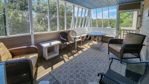 A covered patio with wicker furniture, a ceiling fan, and large windows offering views of trees. - Fair Winds - Oceanside home w/Private Pool - Dogs Allowed! (Southern Shores)