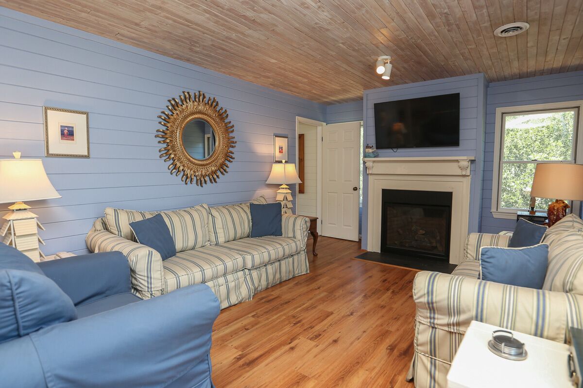 A living room with striped sofas, a fireplace, and a television mounted above it.