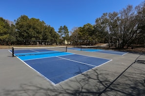 An outdoor tennis court with a net in the middle, surrounded by trees and a fence.