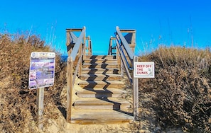 A wooden staircase leading to a beach with a 'Keep Off the Dunes' sign and a 'Sea Turtle Nesting Season' informational sign.