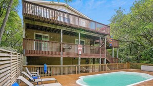 Una casa de madera de dos pisos con piscina, sillas de deck y un letrero que prohíbe el clavado.
