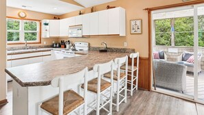 Una cocina con armarios blancos, encimera de granito y una zona de bar con sillas blancas.