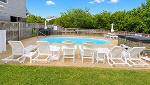 Un patio trasero con piscina, sillas de descanso blancas y cerca de madera.