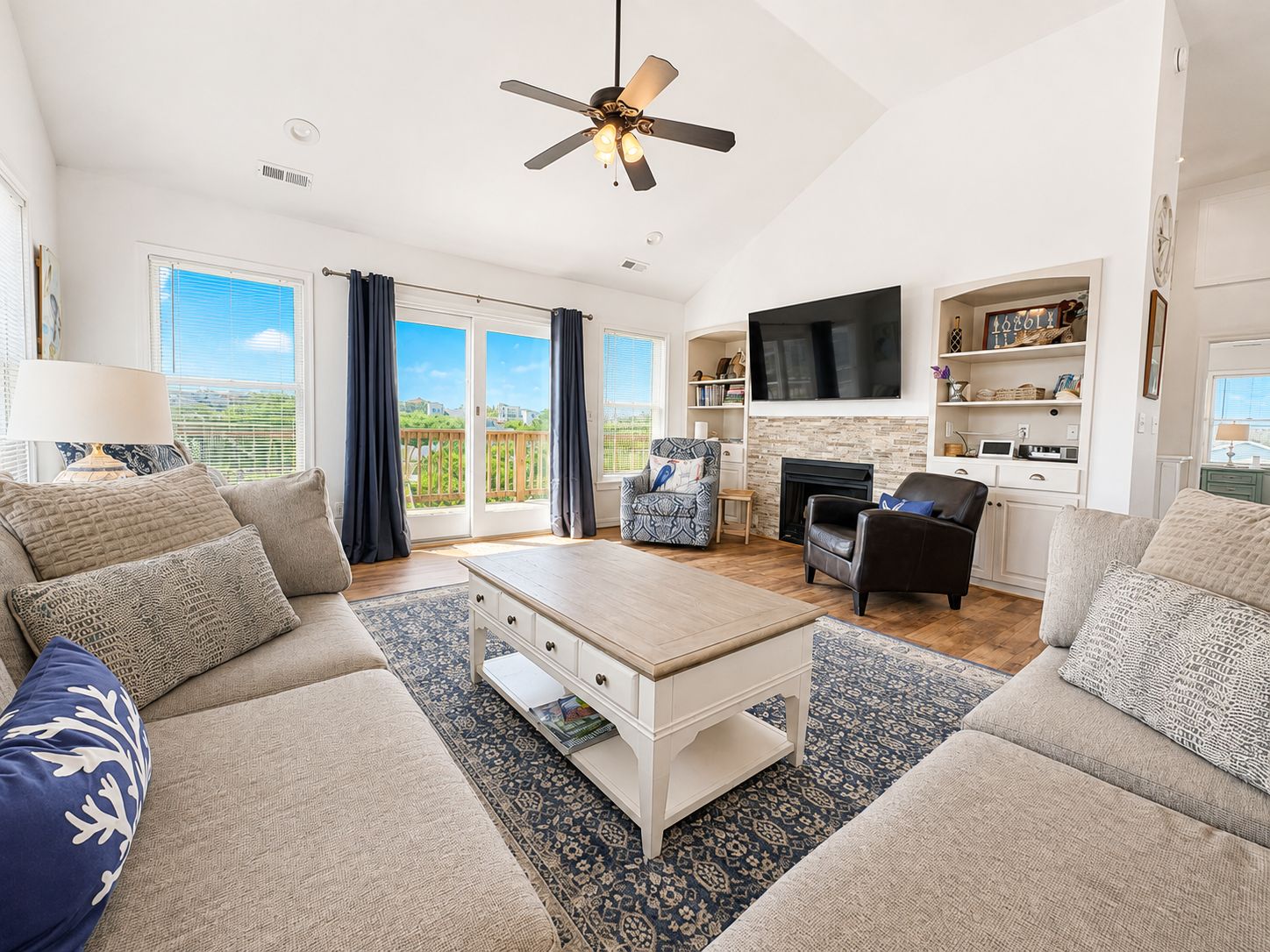 A spacious living room with a ceiling fan, a fireplace, a flat-screen TV, and a large window with curtains.