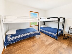 A room with two bunk beds, wooden flooring, a window with blinds, and a framed picture on the wall.