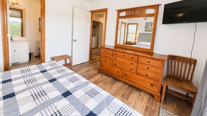 Un dormitorio con cama, cómoda, televisor y una puerta que da al baño.
