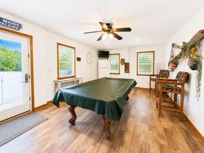 A pool table in a room with wooden flooring, a ceiling fan, and a door with a sign.