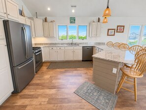 A modern kitchen with white cabinets, a stainless steel refrigerator, a built-in oven, and a granite countertop.
