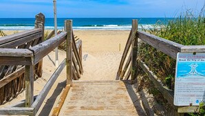 Pasarela de madera que conduce a una playa, con un cartel advirtiendo sobre corrientes de resaca.