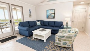 A living room with a blue sofa, a white coffee table, and a patterned armchair. - 12 ON 12 - Sip coffee and take in the beautiful ocean views with this oceanfront home! (Southern Shores)