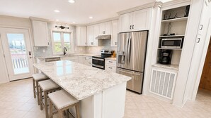 A modern kitchen with a large island, stainless steel appliances, and a view to the outside. - 12 ON 12 - Sip coffee and take in the beautiful ocean views with this oceanfront home! (Southern Shores)