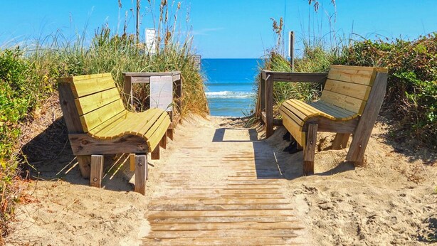 A wooden pathway leading to beach chairs on a sandy beach with the ocean in the background. - Knock On Wood - Directly across from the beach access with terrific ocean views (Duck)