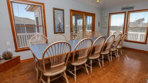 A dining room with a long table and six chairs, large windows with blinds, and a 'Welcome' sign on the wall.