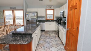 A kitchen with white cabinets, a granite countertop, and a wooden door. - Peachy Plover - Oceanside 6 BR Home w/Private Pool & Hot Tub (Duck)