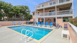 A swimming pool with lounge chairs and a two-story building with balconies. - Peachy Plover - Oceanside 6 BR Home w/Private Pool & Hot Tub (Duck)