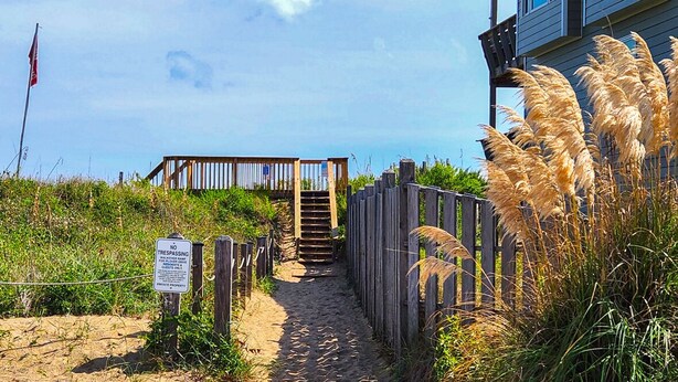 A sandy beach path leading to a wooden staircase with a 'No Trespassing' sign. - Peachy Plover - Oceanside 6 BR Home w/Private Pool & Hot Tub (Duck)