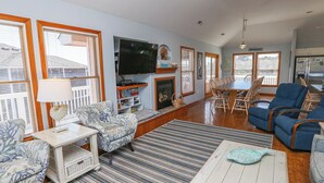 A spacious living room with a fireplace, a dining area, and a kitchen. - Peachy Plover - Oceanside 6 BR Home w/Private Pool & Hot Tub (Duck)