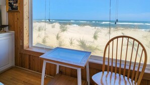 Habitació amb interior de fusta, finestra amb vista a una platja, taula i cadira.