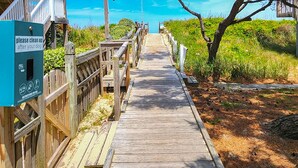 Une promenade en bois mène à une plage où un panneau rappelle aux promeneurs de ramasser les excréments de leurs chiens.