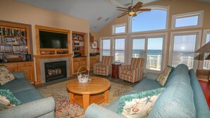 A living room with a fireplace, a television, a bookshelf, and a view of the ocean. - Star Gazer - Wake up to an Outer Banks sunrise from this luxurious oceanfront home (Duck)
