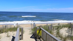A beach with a wooden walkway leading to the shore, a caution sign, and a clear view of the ocean. - Star Gazer - Wake up to an Outer Banks sunrise from this luxurious oceanfront home (Duck)