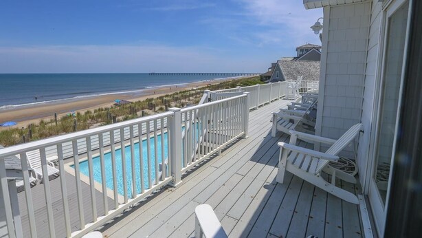 A wooden deck with a pool, beach view, and a pier in the distance. - Star Gazer - Wake up to an Outer Banks sunrise from this luxurious oceanfront home (Duck)