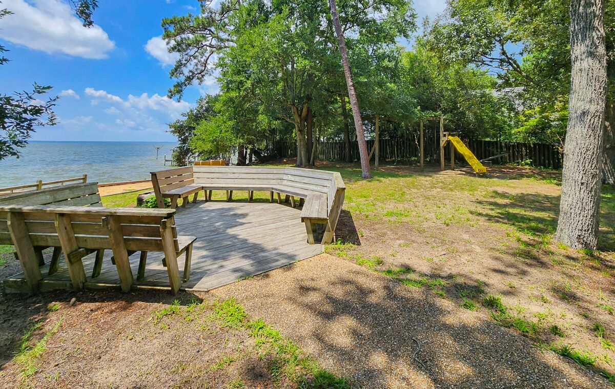 Une terrasse en bois avec des bancs, une aire de jeux avec un toboggan et une vue sur l’eau.