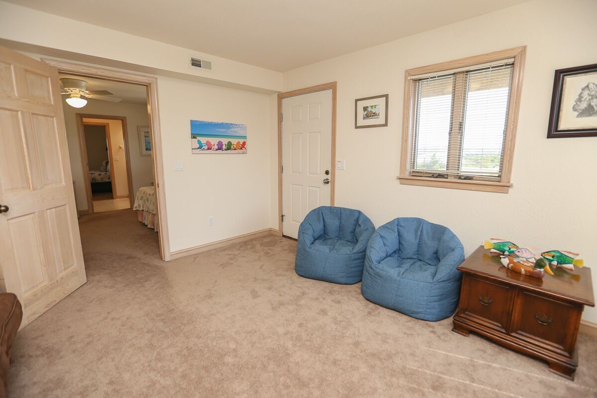 A room with beige carpet, two blue bean bags, a wooden dresser, and a door leading to another room.