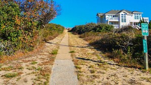 A coastal path leading to a beachfront house with a 'Welcome' sign and a 'No Swimming' sign.