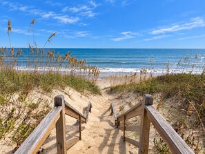 A wooden boardwalk leading to a beach with sand and grass on either side.