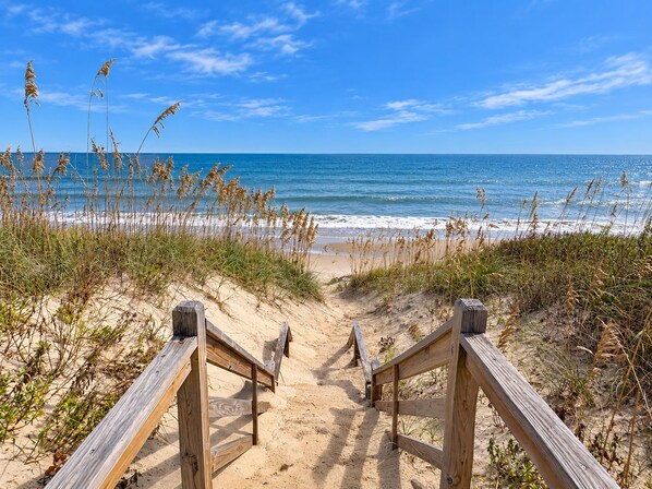 A wooden boardwalk leading to a beach with sand and grass on either side. - Carolina Dreamin' - Oceanfront 5 BR Home with community pool - Dogs Allowed (Duck)