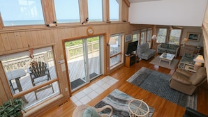 A spacious living area with large windows, a sliding glass door to a deck, and a cozy seating arrangement. - Carolina Dreamin' - Oceanfront 5 BR Home with community pool - Dogs Allowed (Duck)