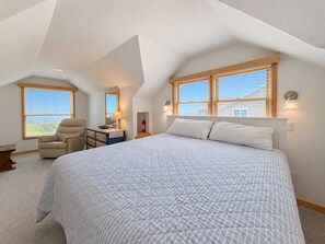 Un dormitorio con una cama grande, una silla, un escritorio y dos ventanas con persianas.