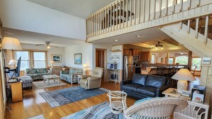 A spacious living area with a high ceiling, a staircase, and a kitchen visible in the background. - Carolina Dreamin' - Oceanfront 5 BR Home with community pool - Dogs Allowed (Duck)