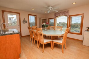 A dining area with a round table, six wooden chairs, a ceiling fan, and large windows with blinds. - Carolina Dreamin' - Oceanfront 5 BR Home with community pool - Dogs Allowed (Duck)