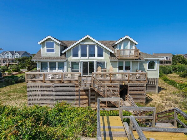 A two-story house with a balcony, a wooden deck, and a staircase leading to the entrance.