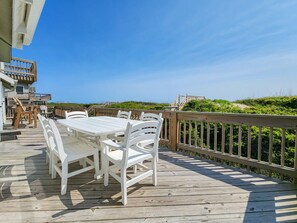 A wooden deck with a white table and chairs, overlooking a beach with greenery. - Carolina Dreamin' - Oceanfront 5 BR Home with community pool - Dogs Allowed (Duck)