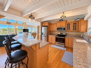 A spacious kitchen with a large island, wooden cabinets, stainless steel appliances, and a view of the beach. - Carolina Dreamin' - Oceanfront 5 BR Home with community pool - Dogs Allowed (Duck)