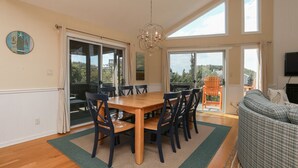 A dining area with a wooden table and chairs, large windows, and a chandelier. - “Surf & Sound” is the best of both worlds! Just steps away from the beach and Sound! (Duck)