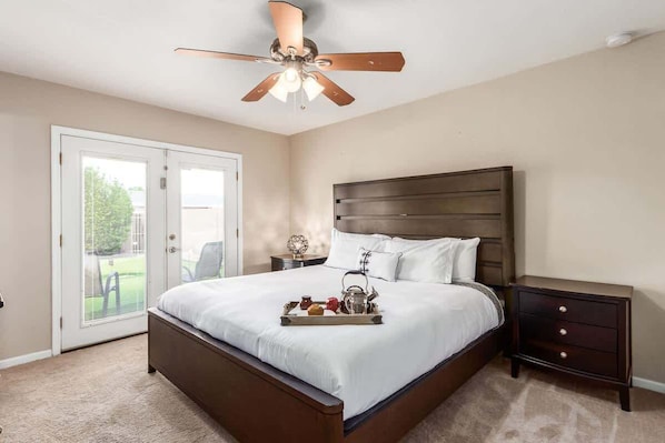 A bedroom with a bed, a nightstand, a ceiling fan, and a sliding glass door.