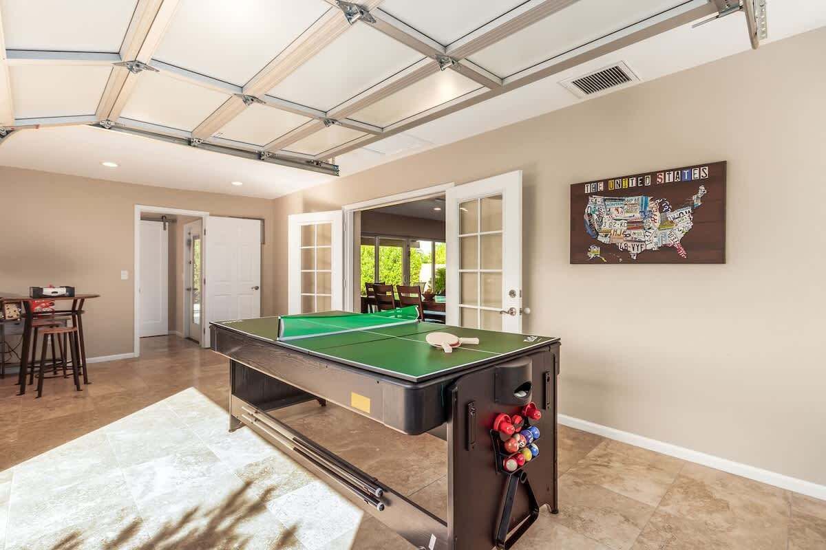 A pool table in a room with a view of the outdoors, a dining area, and a map of the United States on the wall.