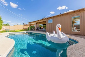 A swimming pool with a swan float, a covered patio area, and a house with a sliding glass door.