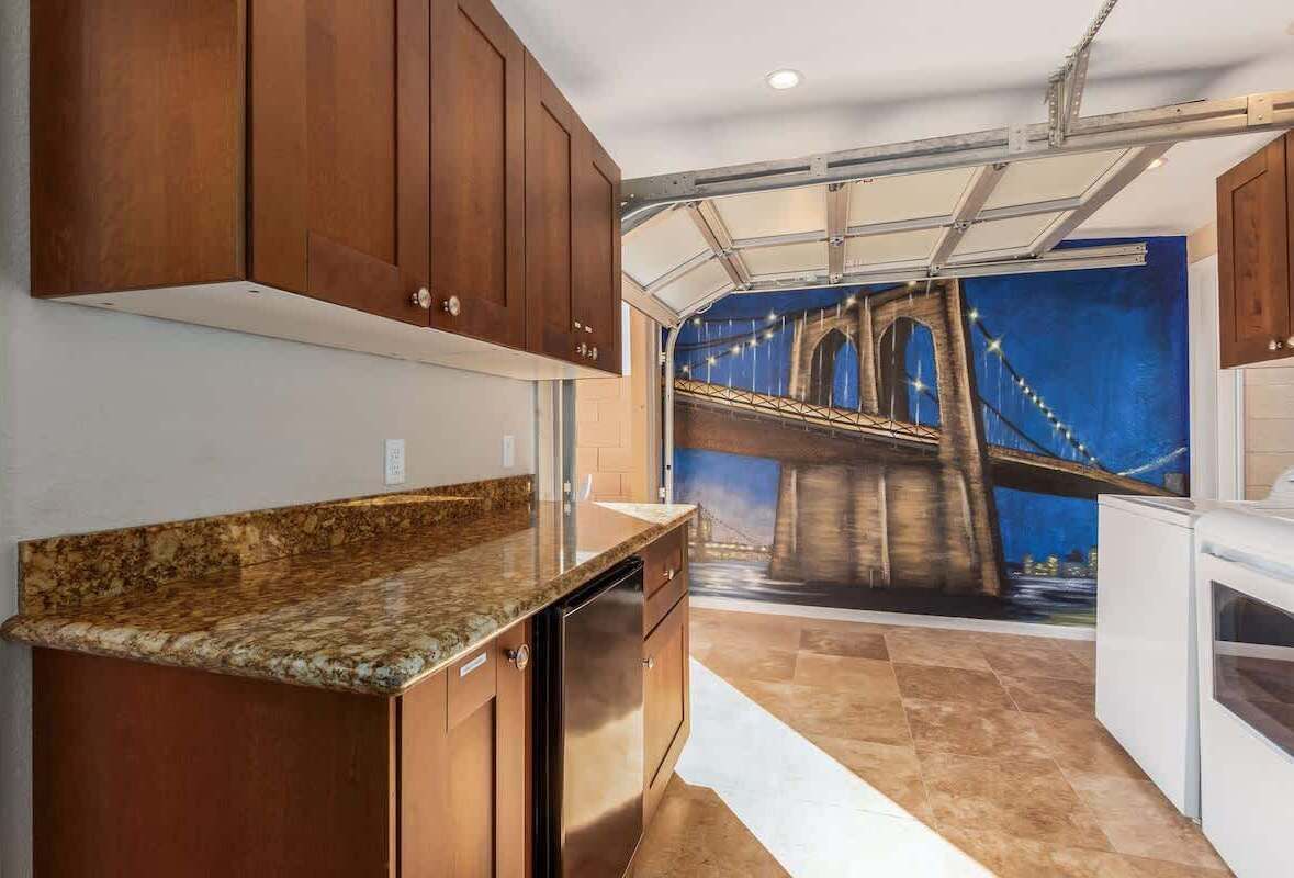 Eine Küche mit Holzausstattung, einer Granit Arbeitsplatte und einem Wandbild einer Brücke.