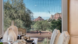A dining area with a table set for two, overlooking a scenic view of red rock formations and trees. - Red Rock-view Sedona retreat with 2 bedrooms, 2 baths, and fireplace. (Sedona)