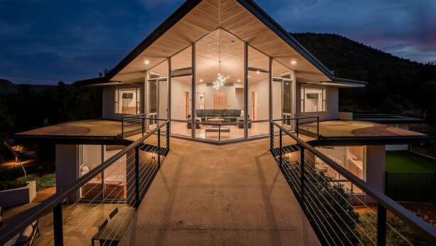 A modern house with a large glass facade, a central living area with a sofa and coffee table, and a staircase leading to a balcony. - Red Rock-view Sedona retreat with 2 bedrooms, 2 baths, and fireplace. (Sedona)