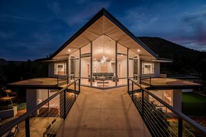 A modern house with a large glass facade, a central living area with a sofa and coffee table, and a staircase leading to a balcony. - Red Rock-view Sedona retreat with 2 bedrooms, 2 baths, and fireplace. (Sedona)