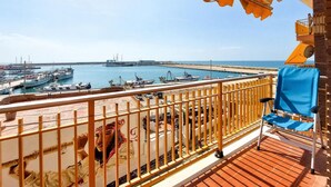 Een balkon met uitzicht op een jachthaven, houten leuningen en een blauwe stoel.
